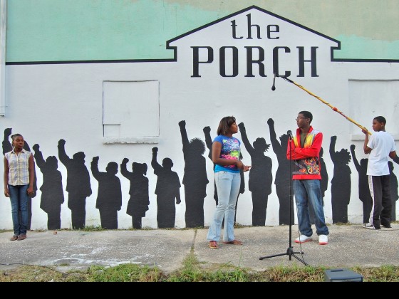 A shot of The Porch's mural shows sillohuettes of children as 3 real life children perform